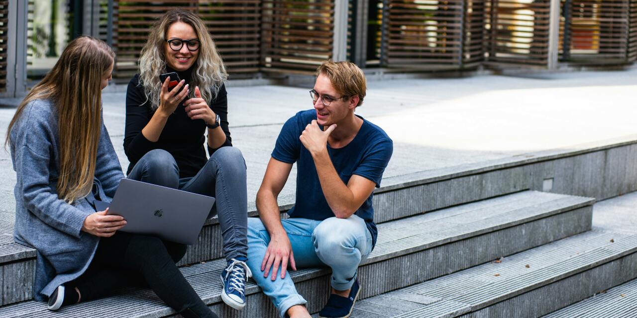 A group of young people gathered on stone stairs sharing a laptop