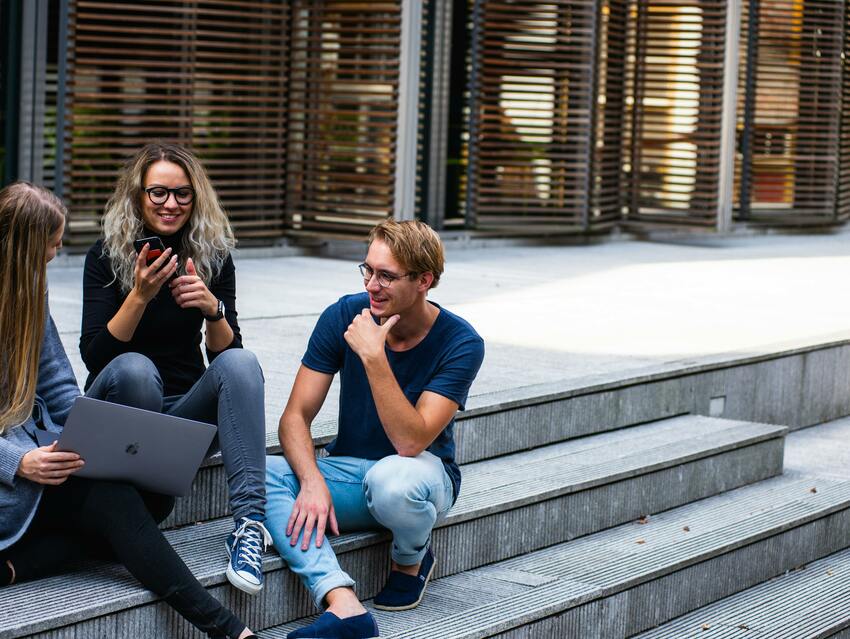 A group of young people gathered on stone stairs sharing a laptop