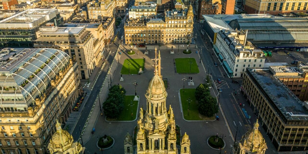 An aerial view looking over the spires of Glasgow City Chambers to George Square and the city centre beyond.