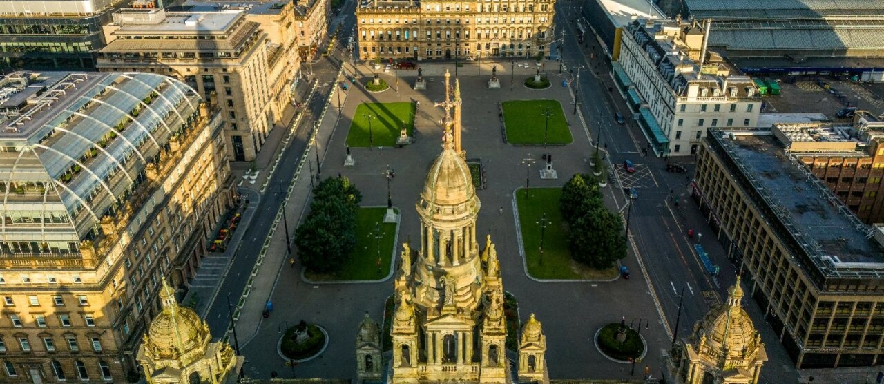 An aerial view looking over the spires of Glasgow City Chambers to George Square and the city centre beyond.