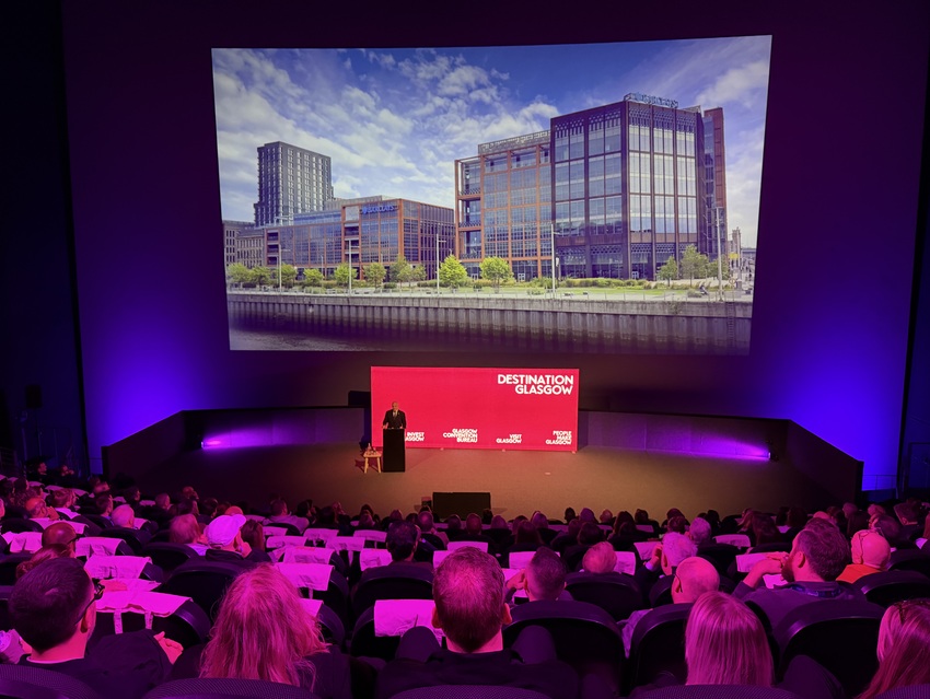 Kevin Rush, Executive Director of Economic Growth, Glasgow City Council, addressed the audience. Kevin is standing at a lectern in front of large pink screen.